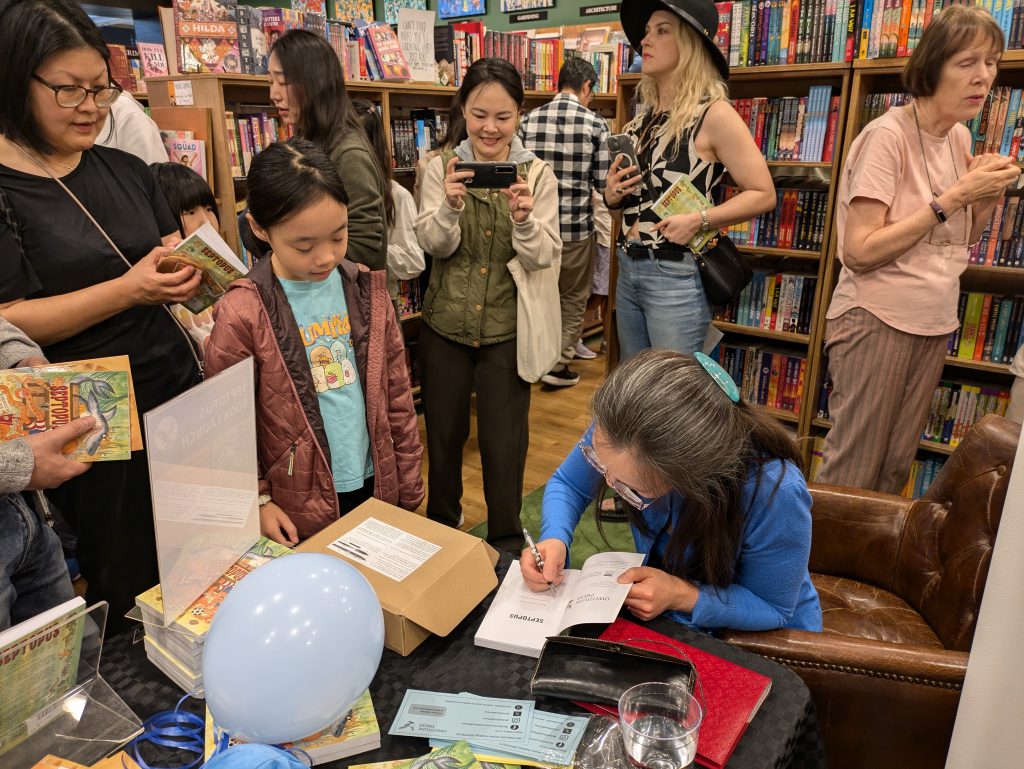 Signing table with a bit of a crowd, author signing book while young girl waits